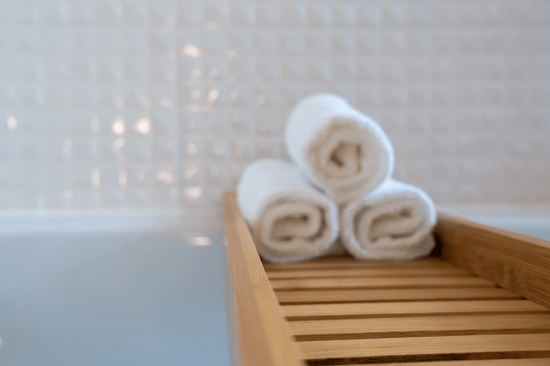 Three rolled towels placed on a wooden rack in a bathtub