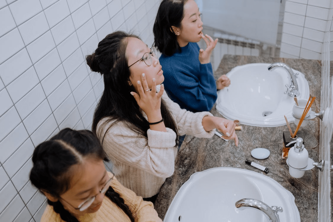 Three young girls applying makeup inside the bathroom