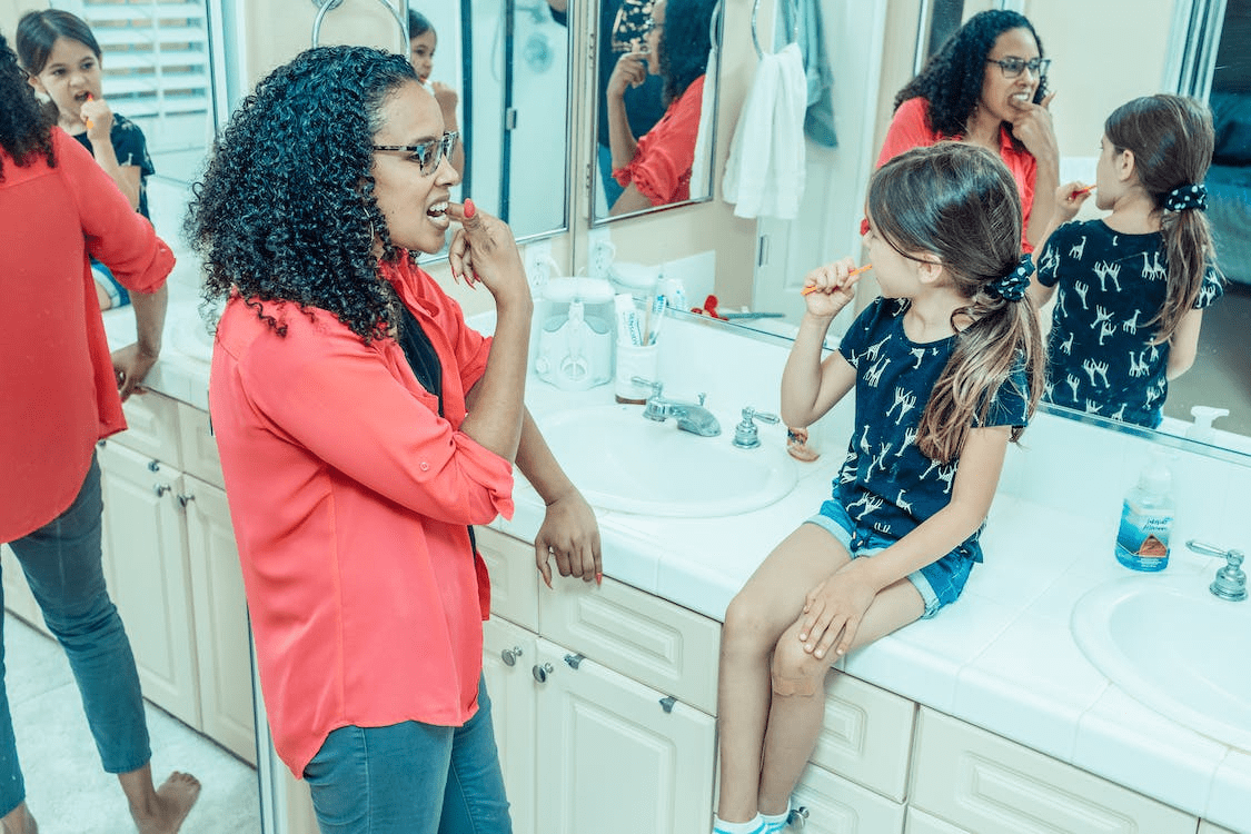 A mother teaching her daughter how to brush her teeth while sitting on the sink