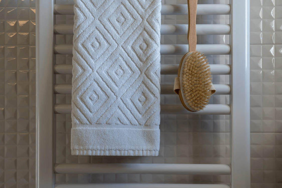 A white towel and a wooden brush hanging on a ladder in the bathroom
